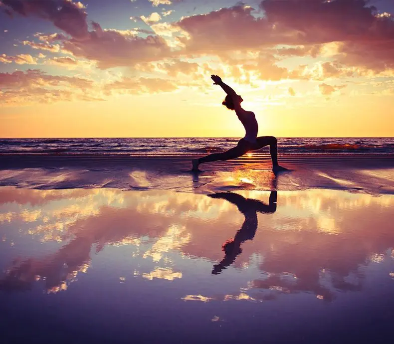 A person doing yoga on the beach at sunset